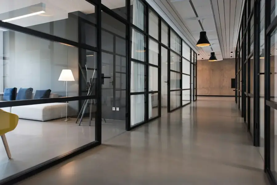 Siyah çerçeveli cam bölmelerle ayrılmış bir ofis koridoru.